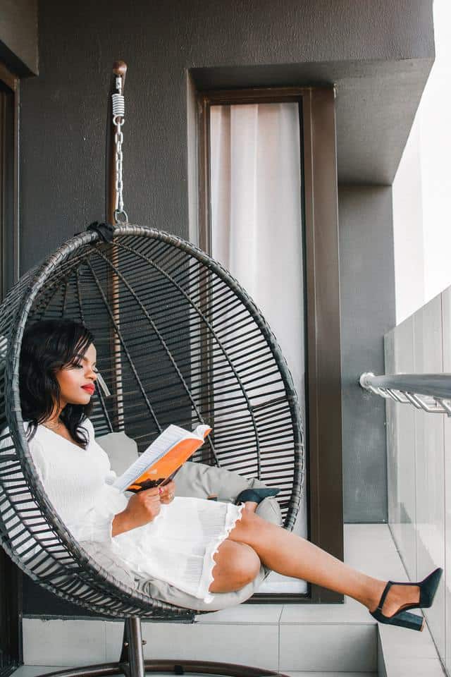 Woman reading book in hammock chair on balcony.