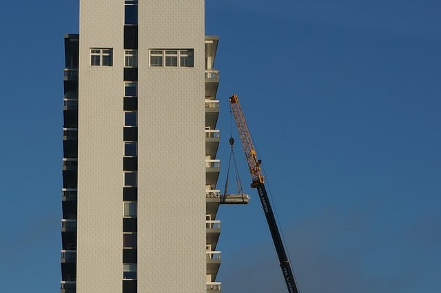 Image shows high rise building with crane hoisting furniture to a balcony. Feature image - hoisting furniture over balcony