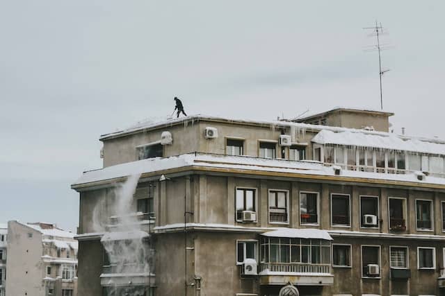 Man on building rooftop shoveling snow.